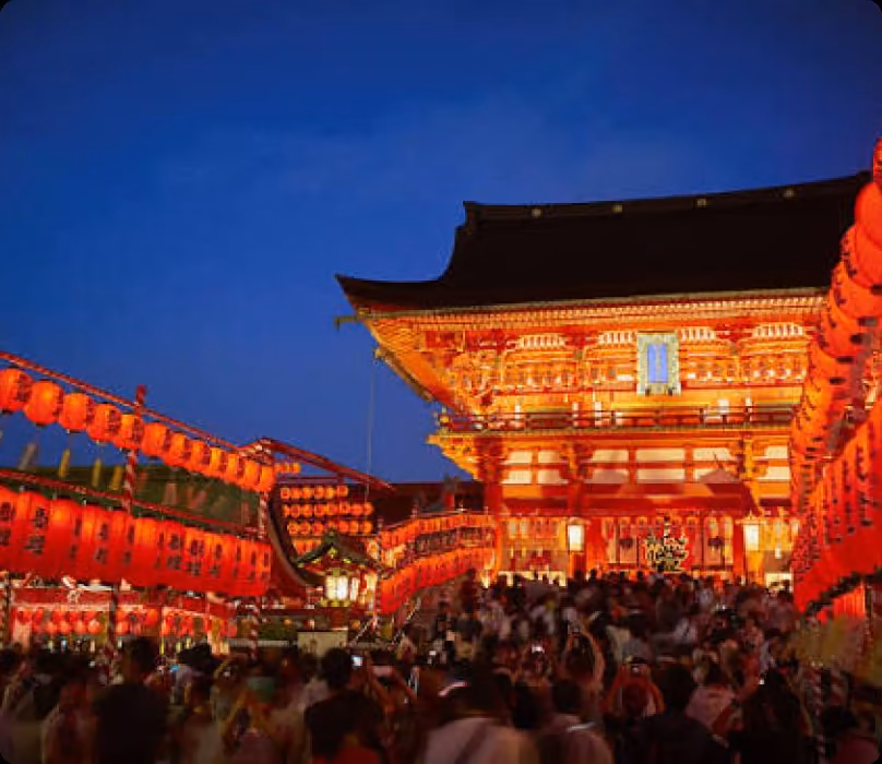 A nighttime festival crowd before a brightly lit shrine gate